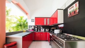 A kitchen with red cabinets, a gas stove, and a window overlooking greenery. - Villa Salines (sleeps 15) Sainte-Anne Jacuzzi Pool, 5 minutes from Pointe Marin (Sainte-Anne)