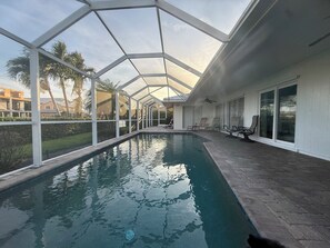 Una piscina coperta con tetto in vetro, circondata da poltroncine e vista su palme.