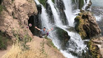A person standing on a rocky ledge with a waterfall behind them.
