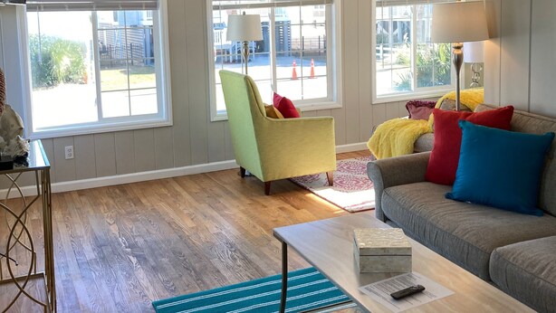 Una sala de estar con sofá, sillón y mesa de centro. Amplias ventanas con vistas al exterior.