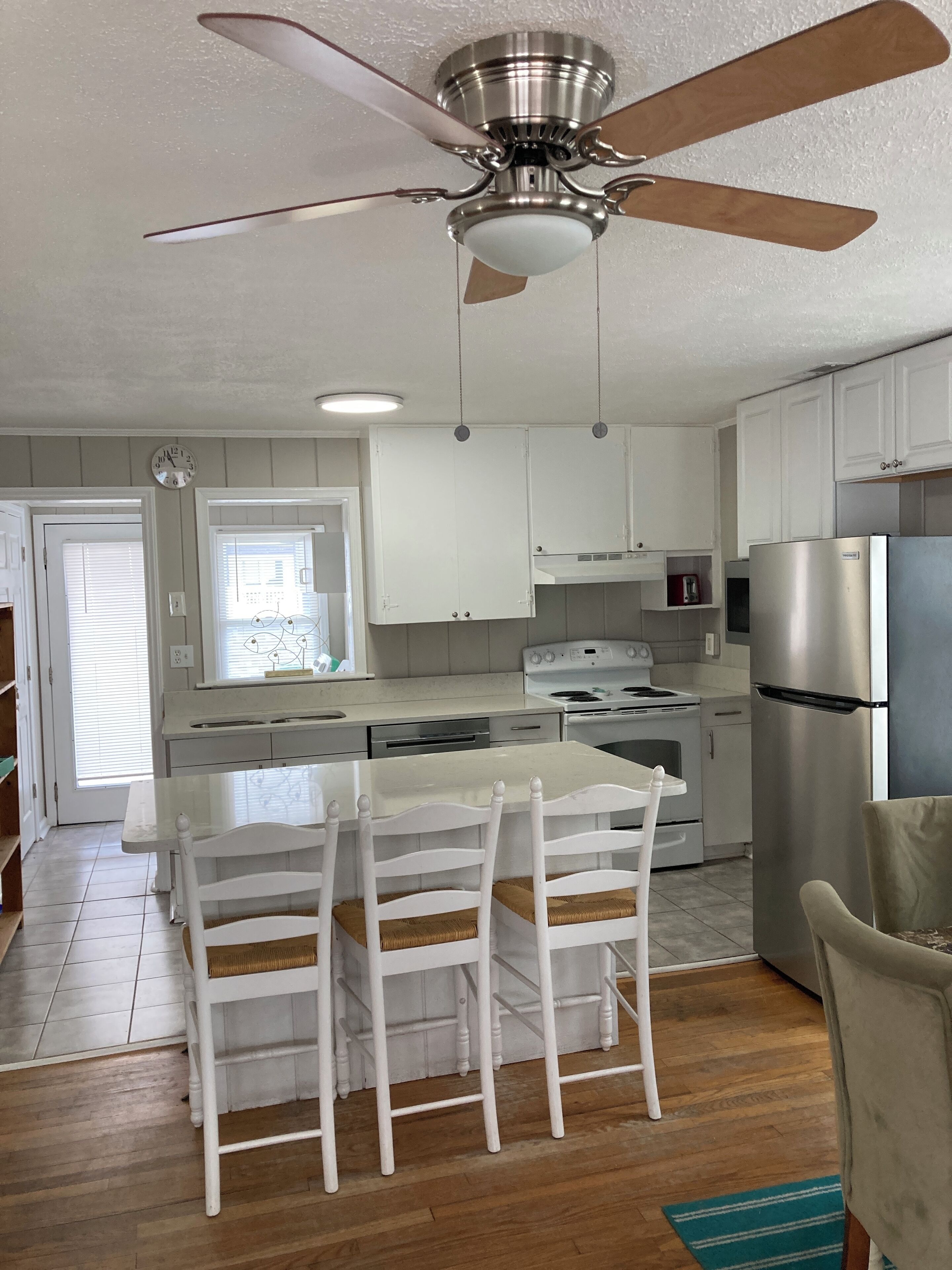 A kitchen with white cabinets, a stainless steel refrigerator, a stove, and a ceiling fan.