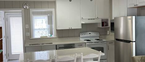 A kitchen with white cabinets, a stainless steel refrigerator, a stove, and a ceiling fan.