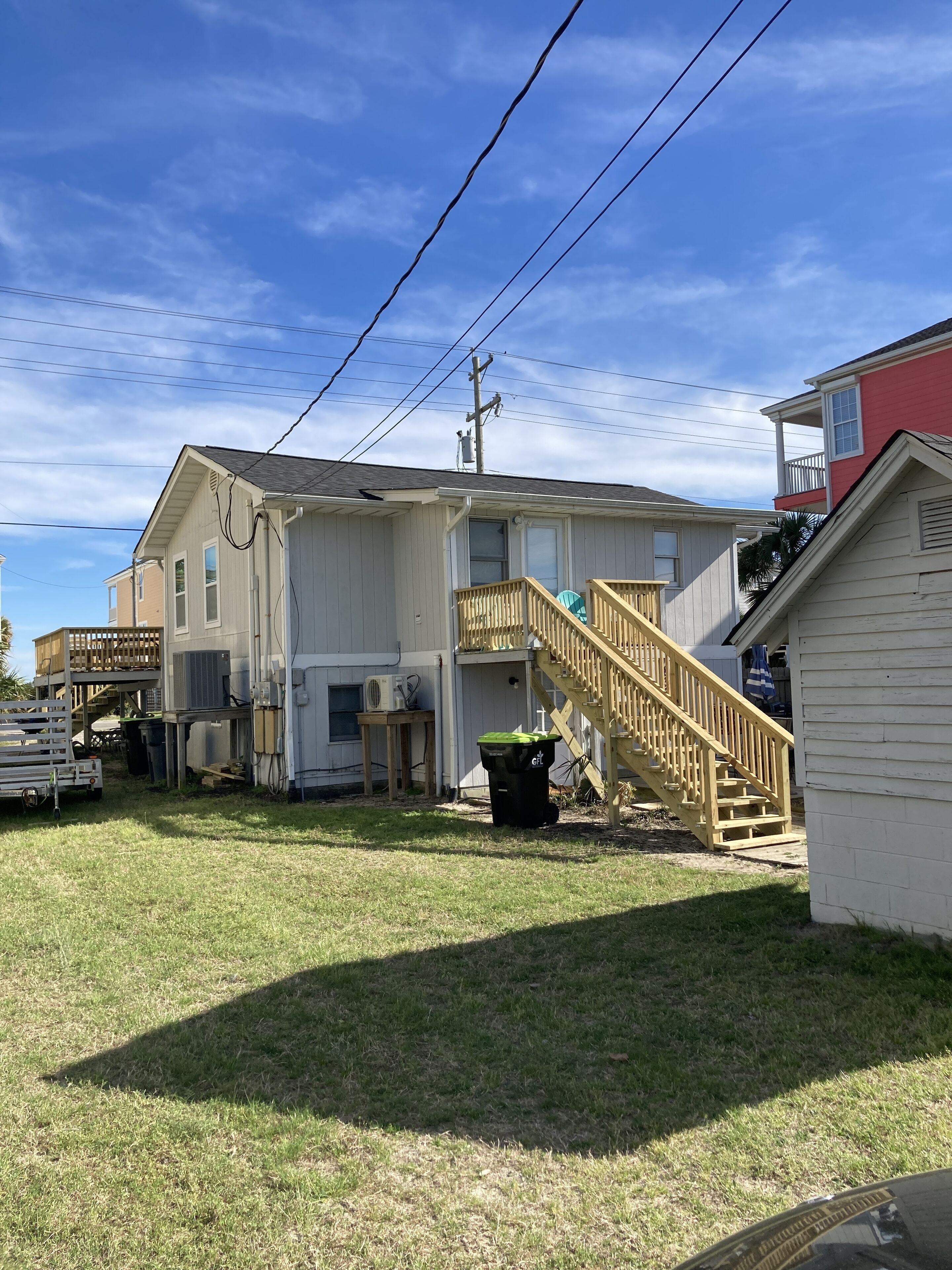A two-story house with a wooden deck, a staircase, and a small shed.
