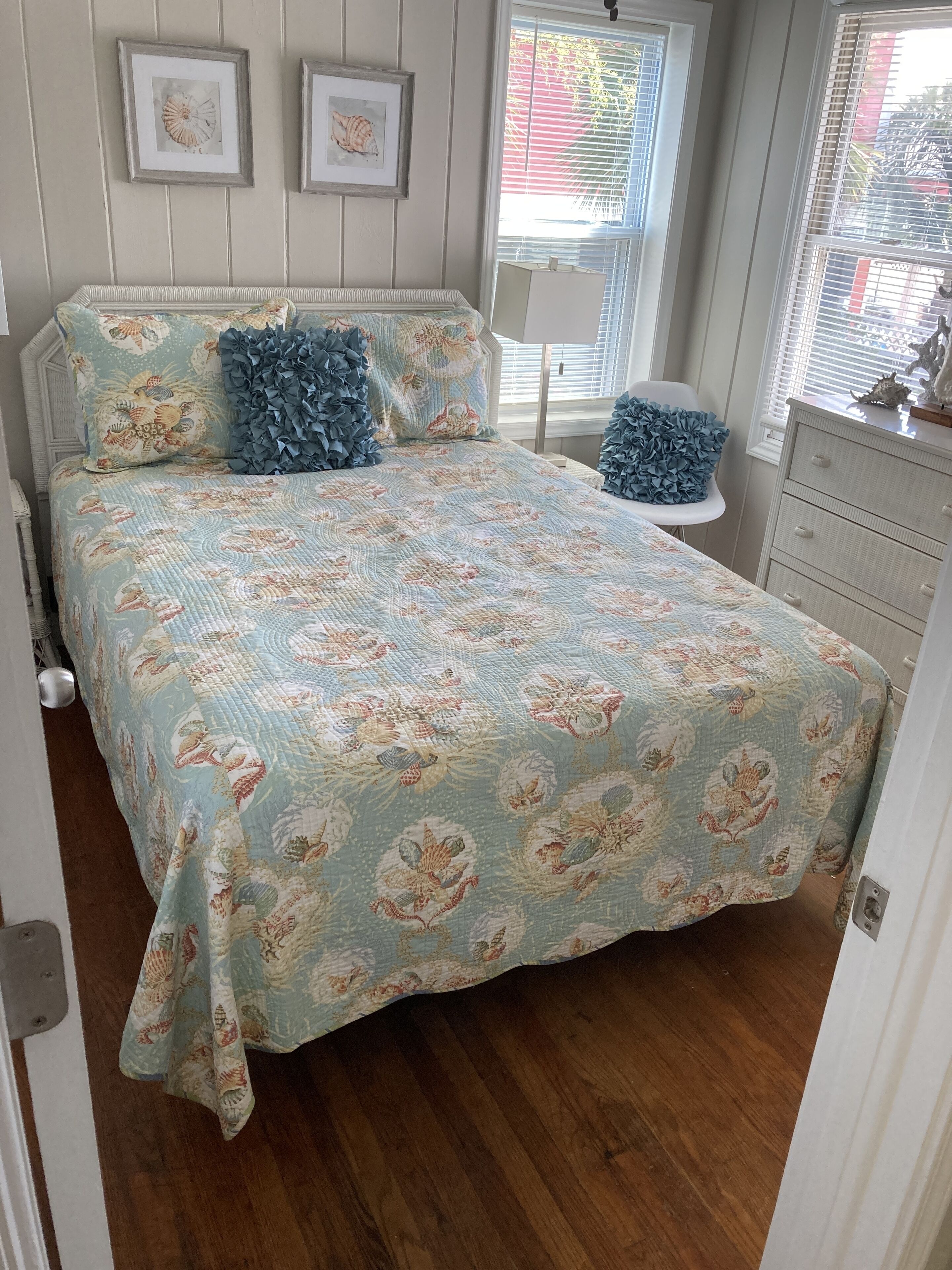 A bedroom with a bed featuring a floral quilt, a dresser, a chair, and framed pictures on the wall.