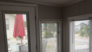 Una habitación con una puerta que da a un espacio exterior, una ventana con persianas y vistas al exterior.
