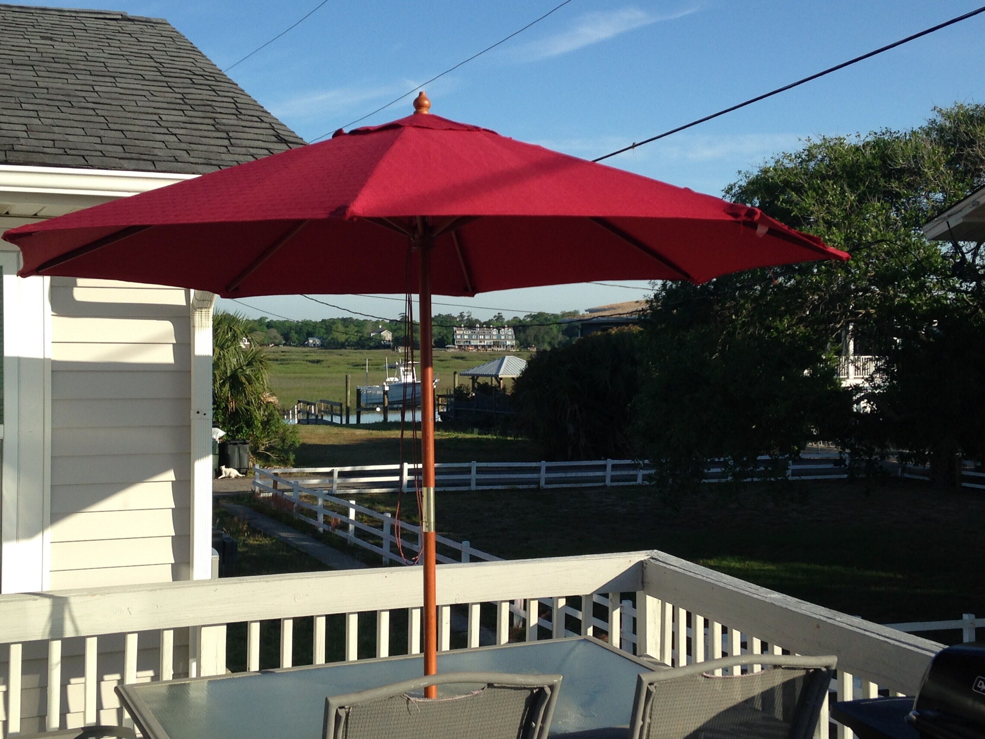 A red umbrella on a porch with a view of a white fence and greenery in the background.