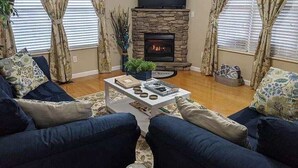 Una sala de estar con chimenea de piedra, un televisor de pantalla plana montado encima y sofás azules.