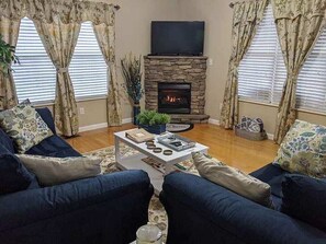 A living room with a stone fireplace, a flat-screen TV mounted above it, and blue sofas. - The Southern Comfort (Pigeon Forge)
