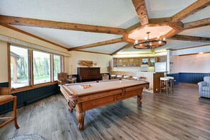 Un'ampia stanza con tavolo da biliardo, travi in legno, ampie finestre, un angolo bar e vista sull'esterno.