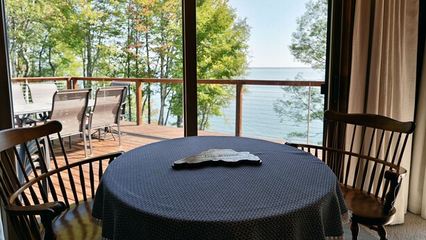 A round table with a dark tablecloth and a decorative piece on it, surrounded by wooden chairs. A large window offers a view of a body of water and trees. - Lake Shore Home with private dock and large deck--1 mile from Bayfield (Bayfield)