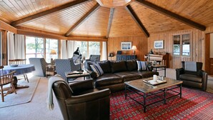 A spacious living room with a high wooden ceiling, leather sofas, a dining table, and a patterned rug. - Lake Shore Home with private dock and large deck--1 mile from Bayfield (Bayfield)