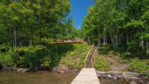 A wooden dock leading to a cabin surrounded by dense forest and a river. - Lake Shore Home with private dock and large deck--1 mile from Bayfield (Bayfield)
