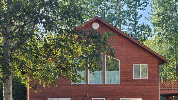A wooden cabin with a sloped roof, a central door, and two windows on the front. There are two Adirondack chairs and a small table with potted plants outside. - Your Home Away from Home in the Heart of the Kenai Peninsula (Soldotna)