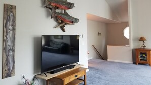 A living room with a flat-screen TV on a wooden stand, mounted fish on the wall, and a staircase leading to another room. - Your Home Away from Home in the Heart of the Kenai Peninsula (Soldotna)