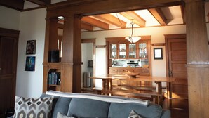 A cozy living room with a wooden ceiling, a dining area with a wooden table and chairs, and a kitchen with wooden cabinets and a hanging light fixture. - Spacious Craftsman w/ Casco Bay Views. Hot Tub, Patio, Easy Access to Old Port (Portland)