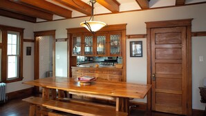 A wooden dining table with benches, a hanging light fixture, and wooden cabinets with glass doors. - Spacious Craftsman w/ Casco Bay Views. Hot Tub, Patio, Easy Access to Old Port (Portland)