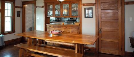 A wooden dining table with benches, a hanging light fixture, and wooden cabinets with glass doors.