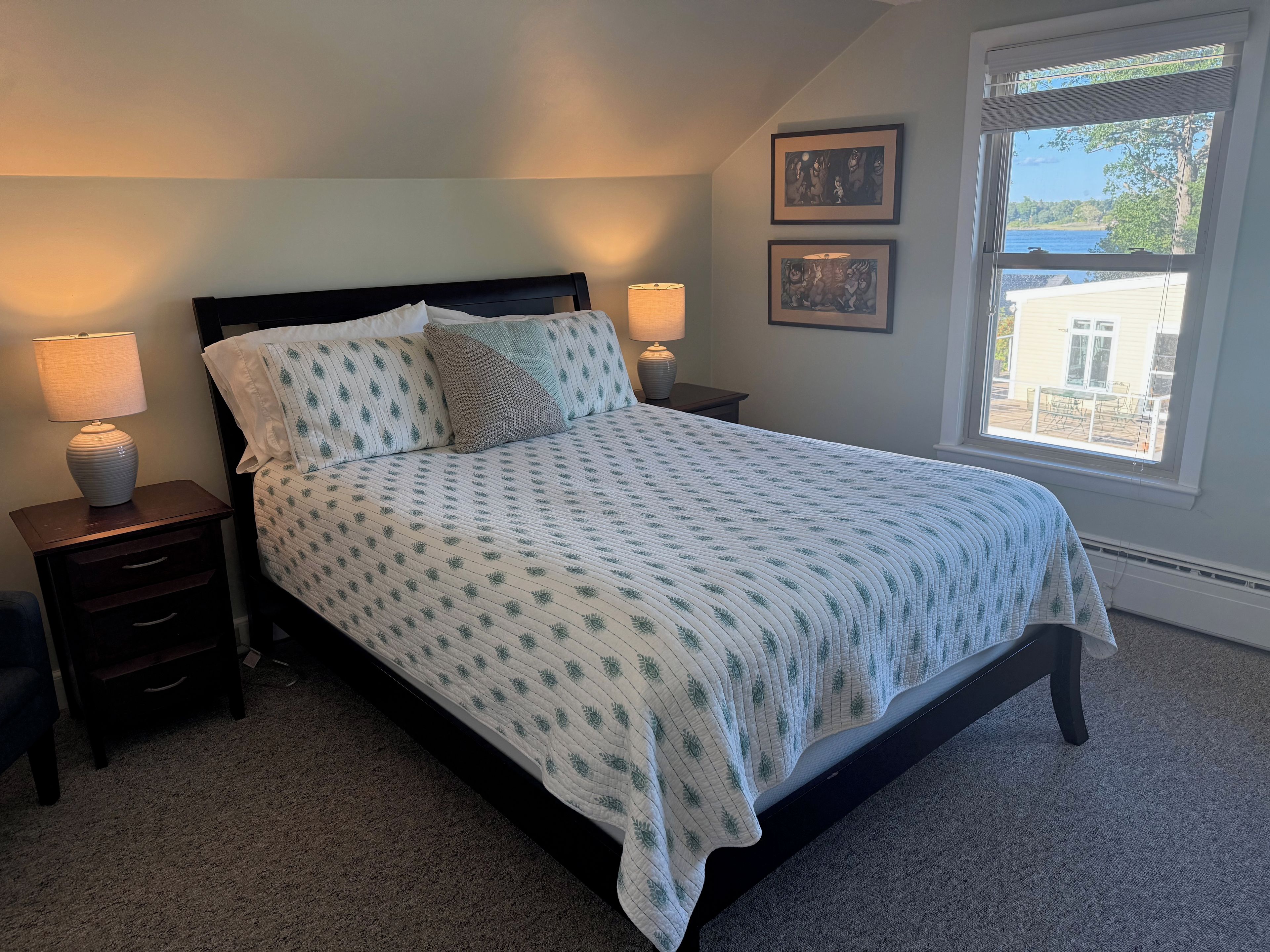 A bedroom with a bed, nightstands, lamps, and a window with a view.
