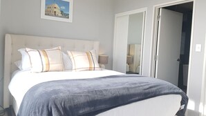 A bedroom with a bed, pillows, a bedside table, and a nightstand. There is a door leading to another room. - Amazing Grace Apartment with Heatpump and Carpark (Auckland CBD)