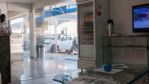 Un hall d’entrée avec une porte vitrée donnant sur l’extérieur, un téléviseur fixé au mur et une table en verre sur laquelle sont posés des journaux et un objet bleu.