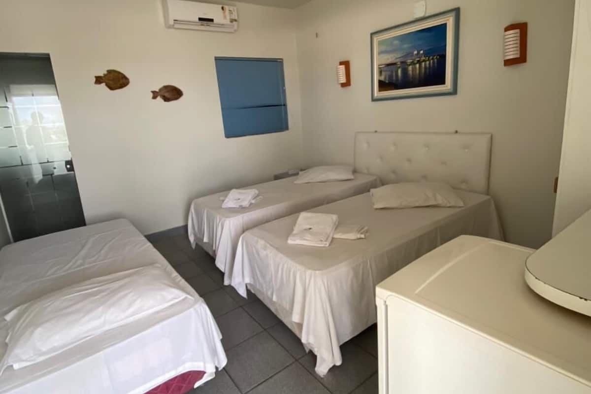 A hotel room with two single beds, a small desk, a mirror, a picture on the wall, and an air conditioning unit.