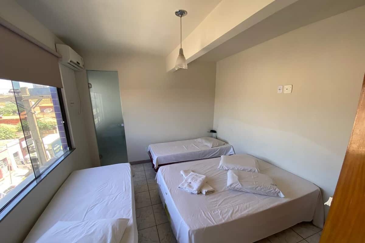 A hotel room with two single beds, a window with a view of buildings, and a ceiling fan.