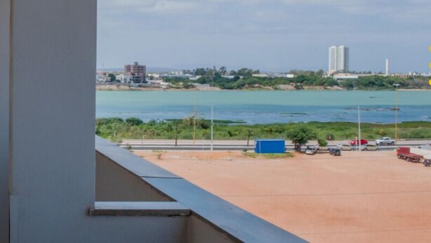 Une vue depuis un balcon donnant sur un parking, avec une étendue d’eau et des bâtiments visibles au loin.