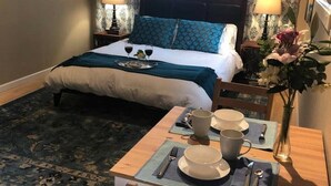 Quarto bem arrumado com uma cama, mesas de cabeceira e um espaço de jantar com uma mesa posta para dois.