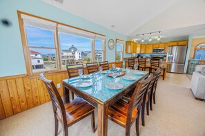 A dining area with a large table, wooden chairs, and a view of houses through large windows. - Soundfront Dog Friendly Home w/ Hot Tub, Game Room, Private Boat Dock, Kayaks (Avon)