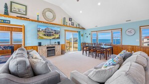 Een ruime woonkamer met een grote televisie, houten meubels en uitzicht op zee.