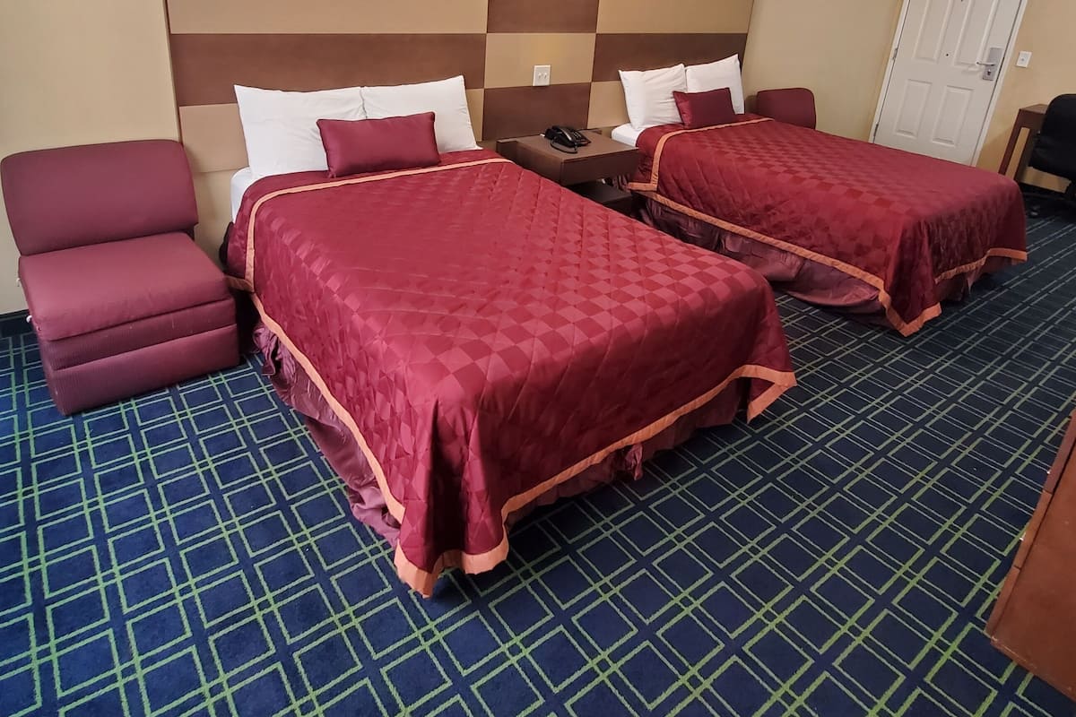 Una habitación de hotel con dos camas, un sillón rojo, una mesita y una puerta.