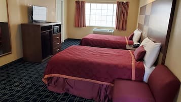 A hotel room with two beds, a desk with a computer, a window with curtains, and a wall-mounted TV.