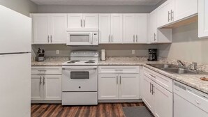 Une cuisine de taille réduite avec des meubles blancs, un four à micro-ondes, une cuisinière et un évier.