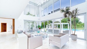 Amplia sala de estar moderna con un gran ventanal que da a una piscina y exuberante vegetación.