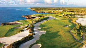 Un campo de golf con búnkeres de arena, una masa de agua y una costa distante.