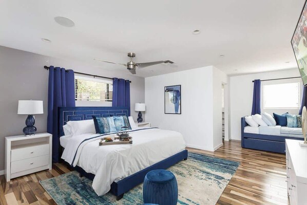 A bedroom with a bed, bedside tables, a ceiling fan, a window with curtains, a sofa, and a rug.