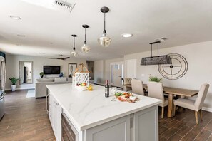 A modern kitchen with a marble island, pendant lights, and a dining area with a wooden table and chairs. - South Scott-Private Pool-Next to Old Town (Scottsdale)