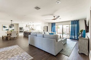 Una sala de estar moderna con sofá, comedor, cocina y un ventanal corredero que da a un espacio exterior.