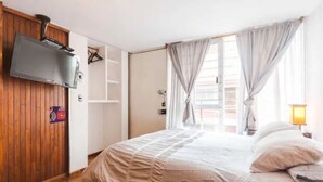 Een slaapkamer met een bed, een tv aan de muur, een kledingkast en een raam met gordijnen.