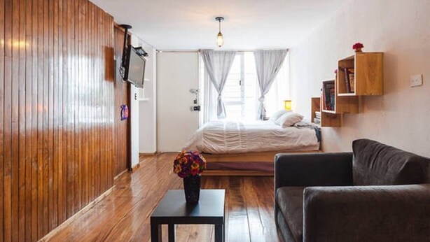 Een slaapkamer met een bed, een televisie, een houten wand, een raam met gordijnen, een nachtkastje en een stoel.