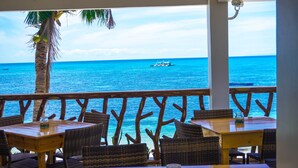 Un ristorante con tavoli e sedie in legno affacciato sull'oceano, con un palmo e vista sul mare.
