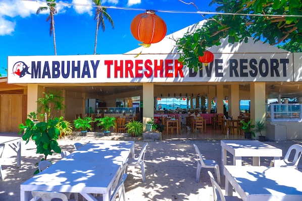 Un restaurante junto a la playa llamado "MabuHay Threshers Dive Resort" con terraza y palmeras.
