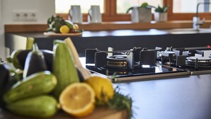 Una cocina con estufa a gas, tabla de cortar con verduras y ventana con plantas.