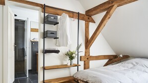 Un dormitorio con cama alta, vigas de madera, un estante con toallas y una peque ña planta.