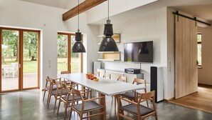 Una cocina moderna con una gran mesa de comedor, sillas de madera, lámparas colgantes y una puerta corredera estilo granja.