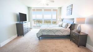 A bedroom with a bed, a TV, a nightstand, and a view of the ocean. - Beautiful Spacious Condo with Wraparound Water and Pool Views with Complimentary Boat Slip! (Orange Beach)