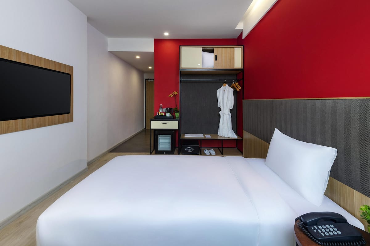 Ein modernes Hotelzimmer mit einem großen Bett, einem Nachttischtelefon, einem Schreibtisch mit Computer, einem Spiegel und einer roten Akzentwand.
