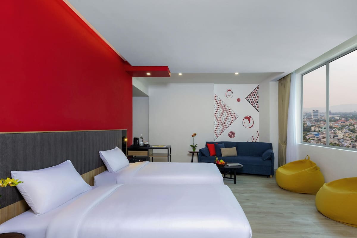 Ein modernes Hotelzimmer mit einem großen Bett, einer Couch, einem gelben Sitzsack und Blick auf die Stadt.