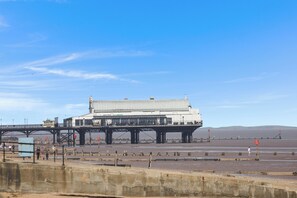 Un edifici gran amb teulada plana i un balcó, sustentat per una estructura metàl·lica negra, amb vista a una zona ampla i oberta sota un cel clar.