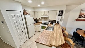 A compact kitchen with white cabinets, a wooden countertop, and a dining area with a table and chairs. - Great St. Augustine beach vacation rental at a family friendly price! (Saint Augustine)